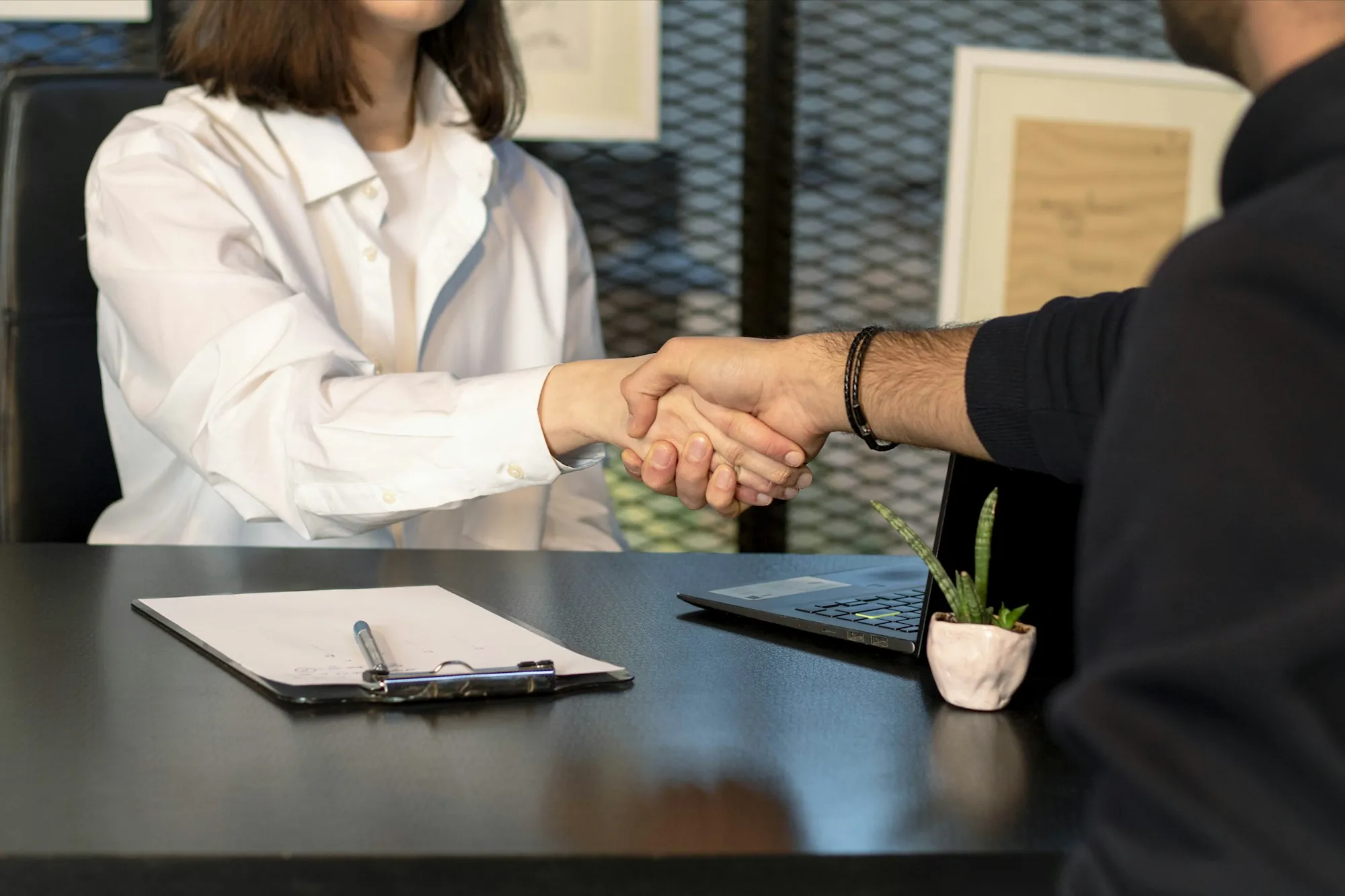 Handshake over a table with a clipboard and documents